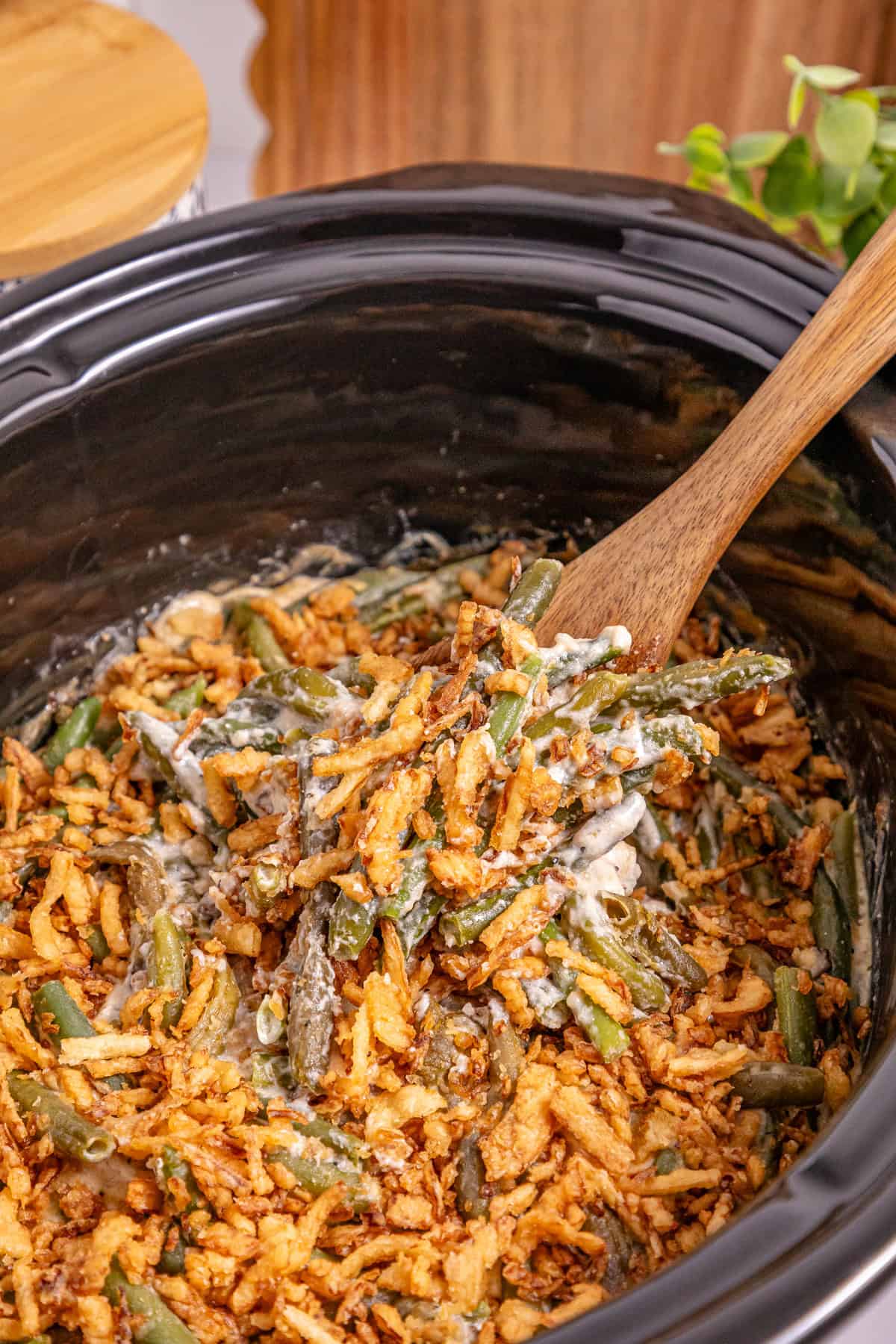 This Slow Cooker Green Bean Casserole is the perfect hands-off side dish for the holidays! Made with just a few ingredients. A wooden spoon stirring slow cooker green bean casserole