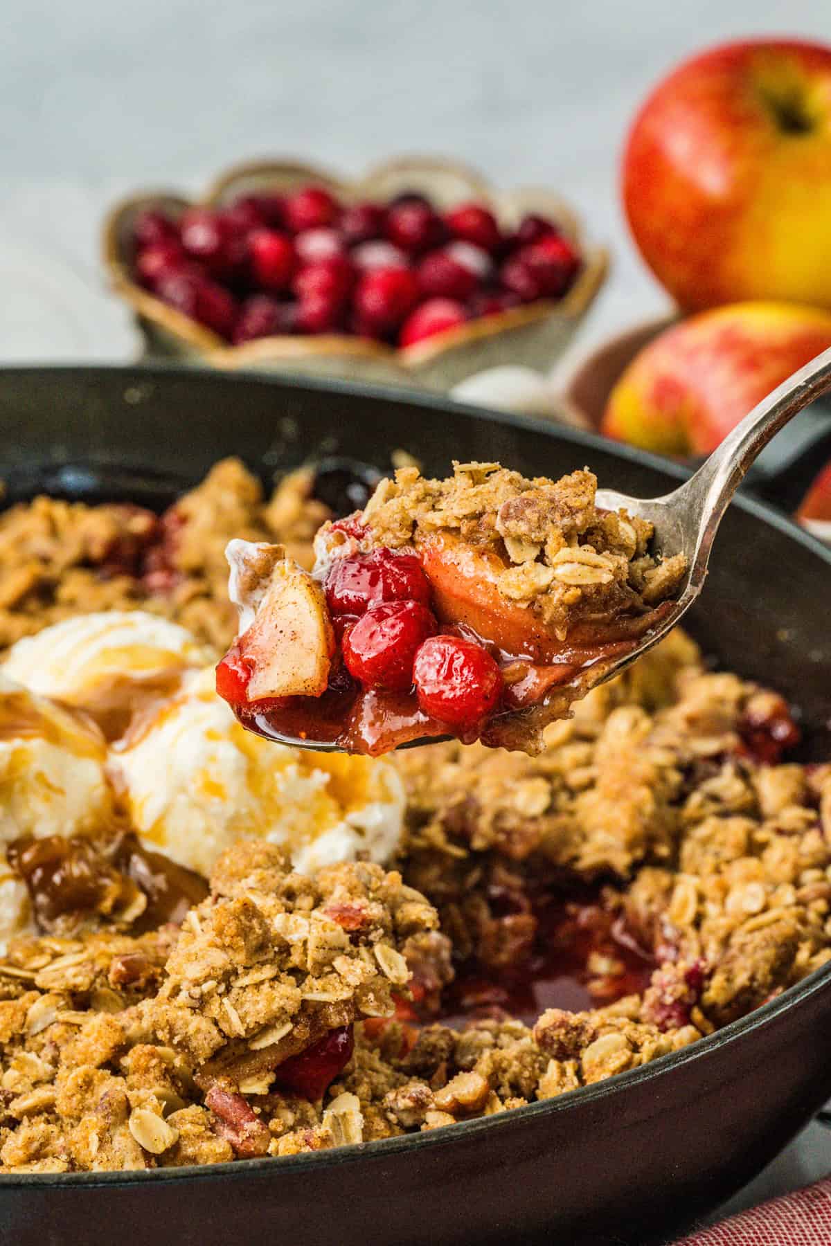 This Apple Cranberry Crisp is baked in a cast-iron skillet, giving the fruit a caramelized edge while the buttery oat turns golden & crunchy. A spoon above a skillet of apple cranberry crisp