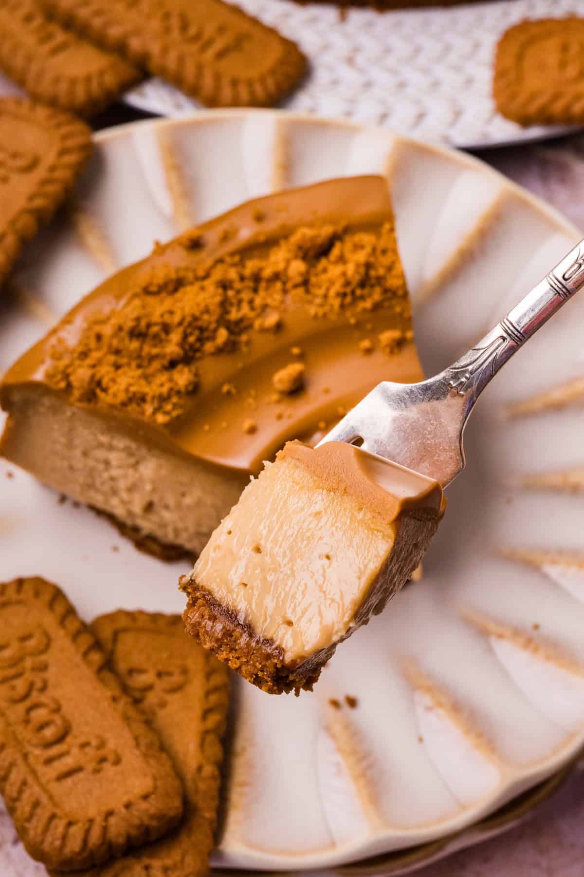 A creamy cookie butter cheesecake filling is baked in a Biscoff crust and topped with more cookie butter in this Biscoff Cheesecake recipe. A bite of Biscoff cheesecake on a plate over a slice