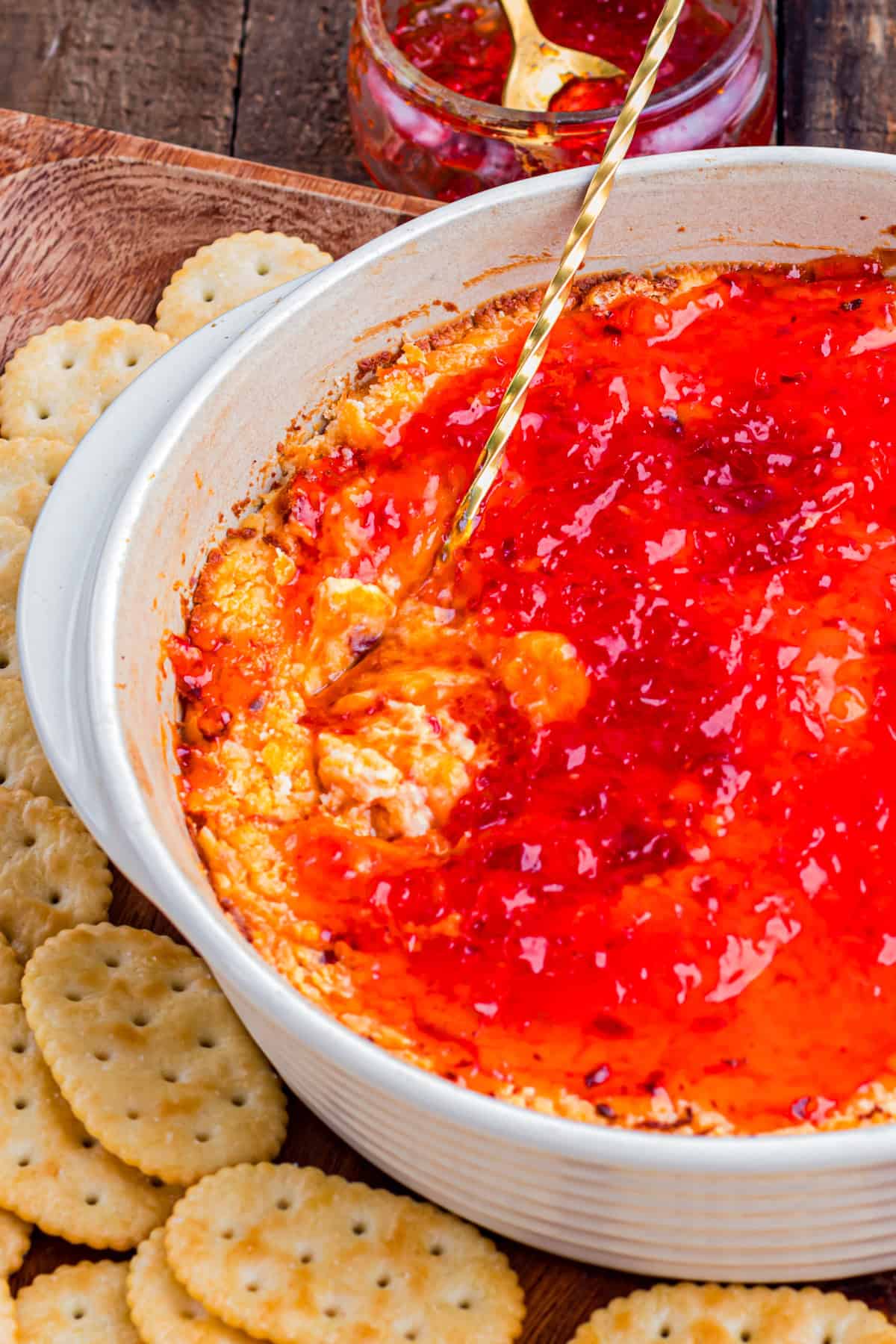 This easy Pepper Jelly Cream Cheese Dip is creamy, cheesy, smoky, and perfectly sweet and spicy! Perfect for holidays & game days. Pepper Jelly Cream Cheese Dip in a baking dish with a spoon.