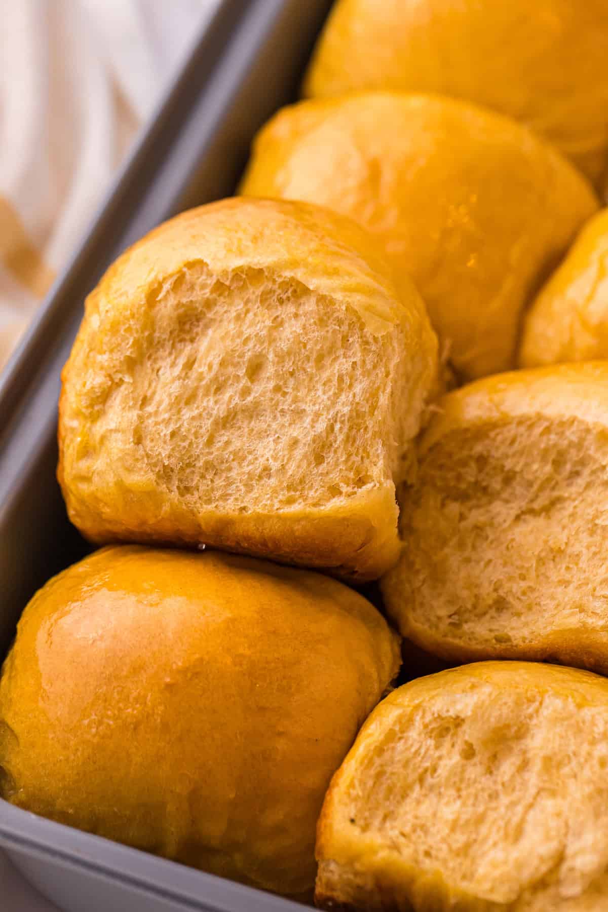 These soft, fluffy Sweet Potato Rolls are brushed with warm honey butter right out of the oven. Easy to make with a few basic ingredients! Sweet potato rolls in a pan, one on its side