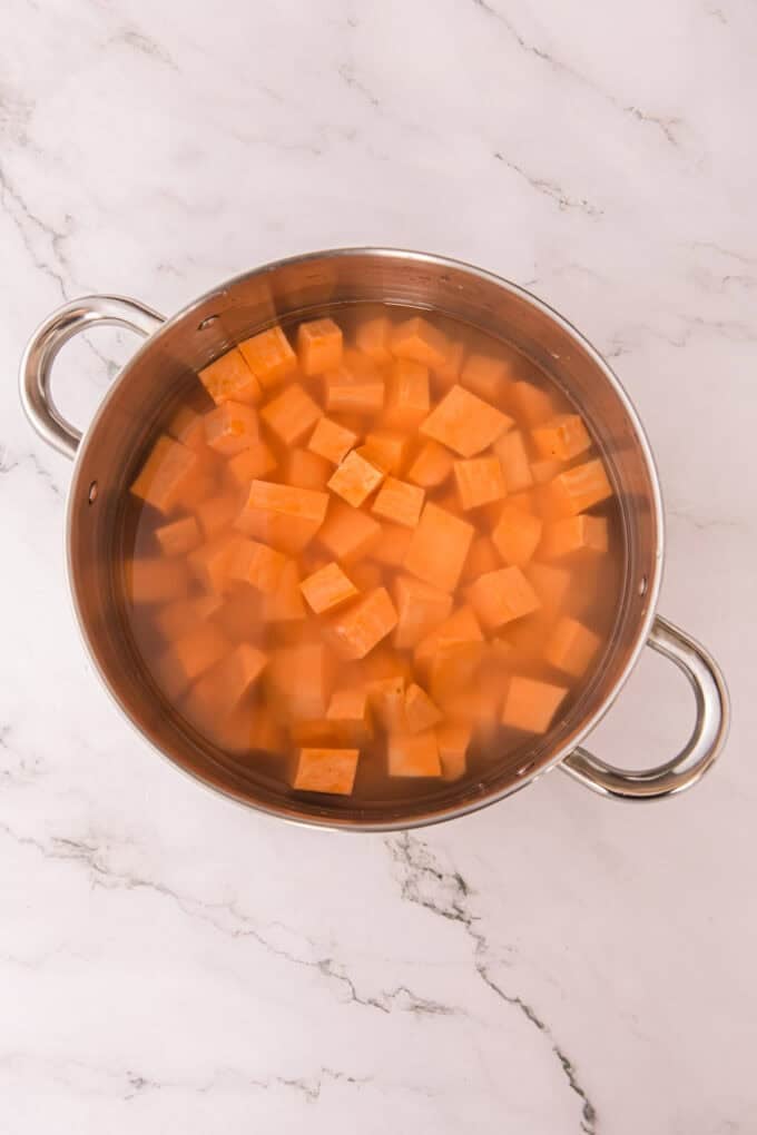 These soft, fluffy Sweet Potato Rolls are brushed with warm honey butter right out of the oven. Easy to make with a few basic ingredients! Cubes of sweet potatoes in a pot of water