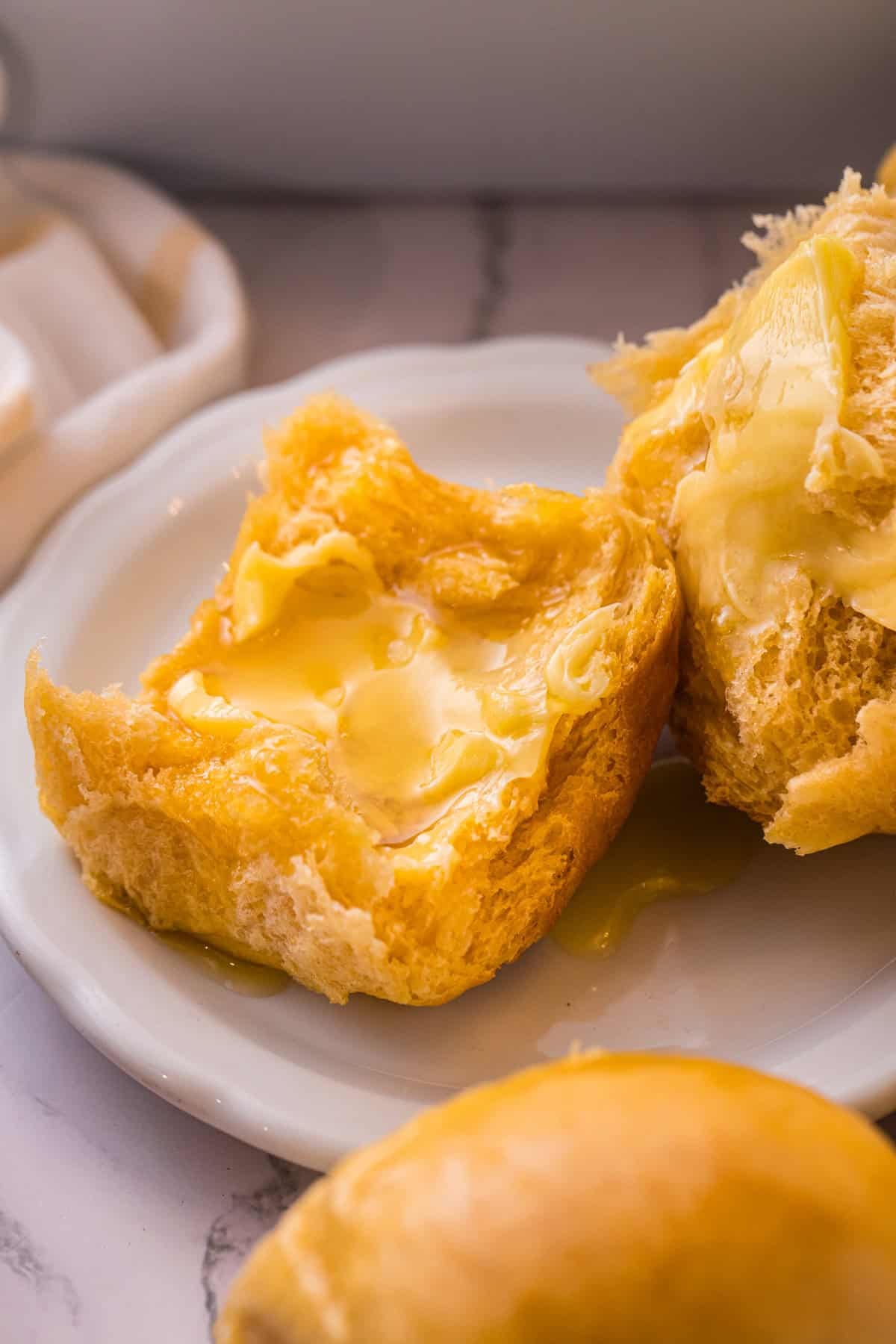 These soft, fluffy Sweet Potato Rolls are brushed with warm honey butter right out of the oven. Easy to make with a few basic ingredients! A sweet potato roll cut in half on a plate with butter